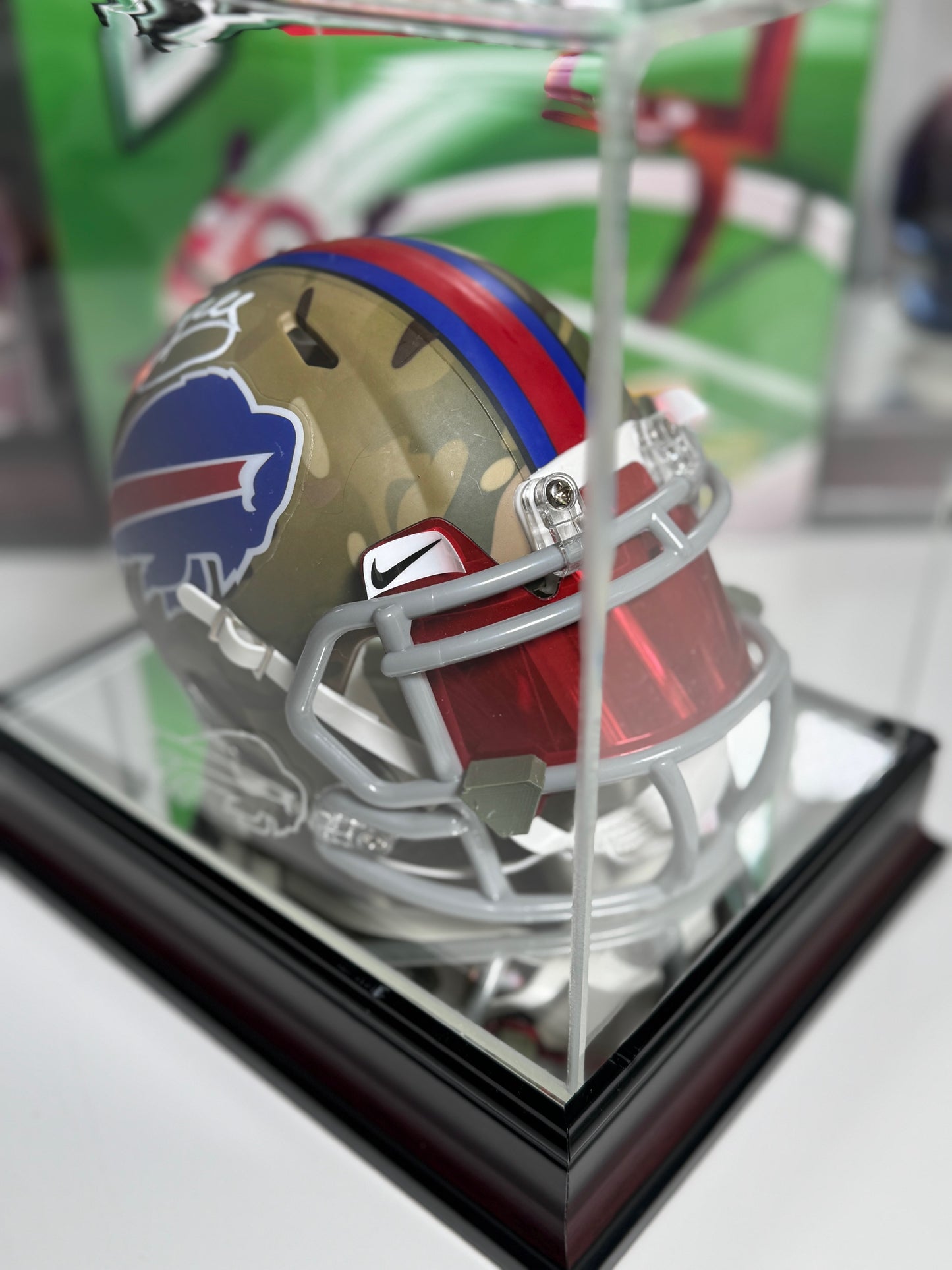 Close-up of Jim Kelly autograph on camo Buffalo Bills mini helmet with red and blue stripe